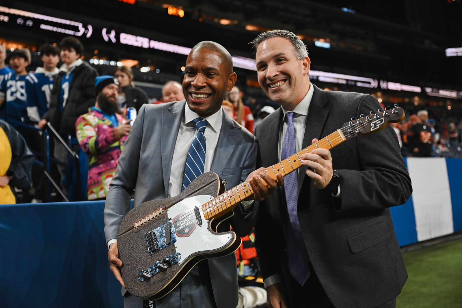 Two people in suits holding the guitar on the sideline