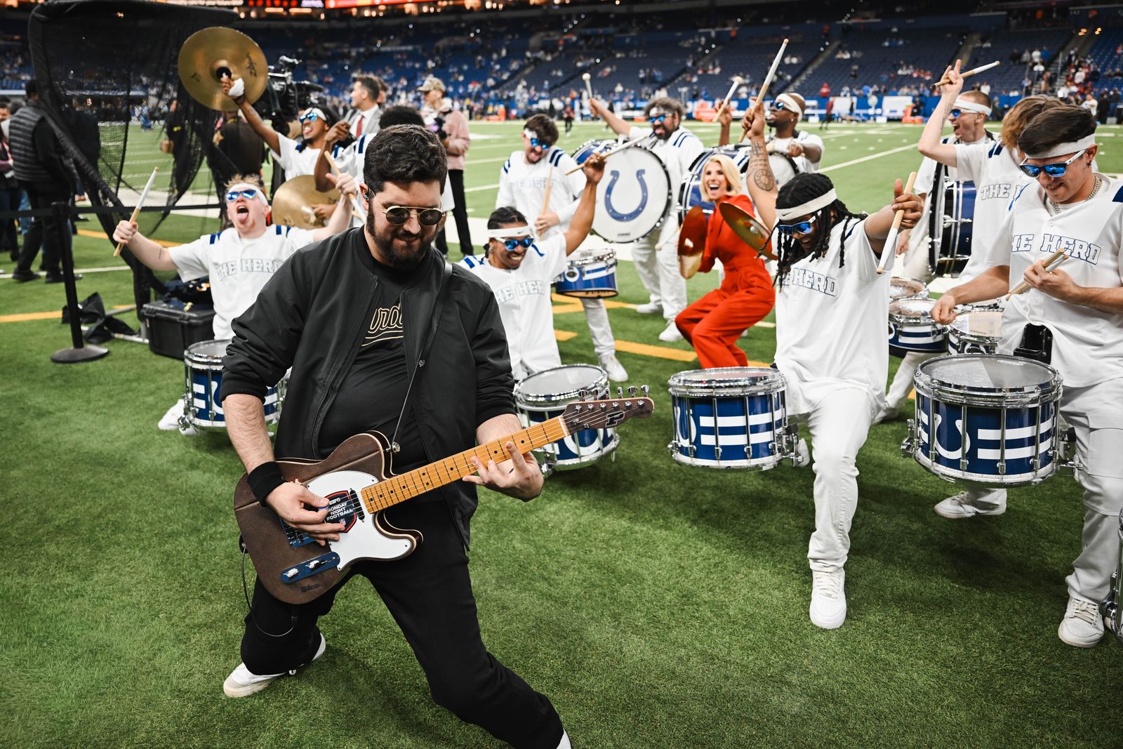 Noah Scott playing the guitar on the field with the Colts drumline around him